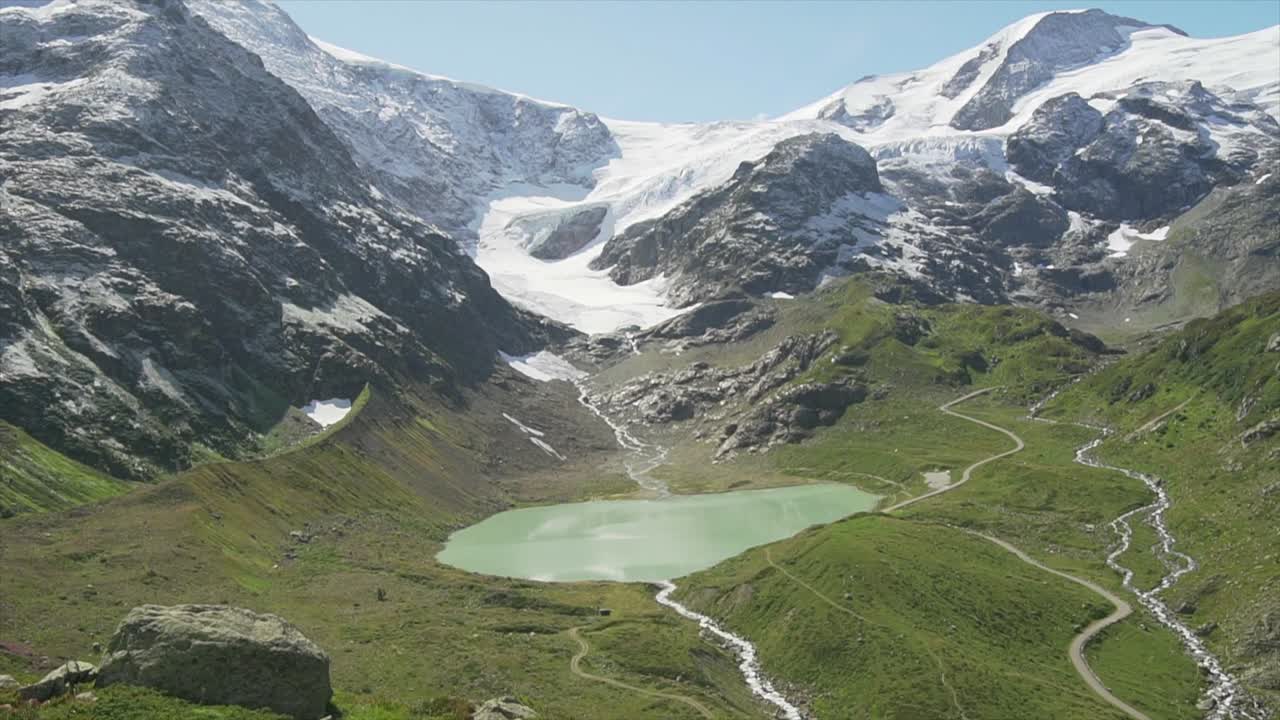 A tilt up shot of a lake, green grass field and a snow capped mountain view in the Swiss Alps in Switzerland