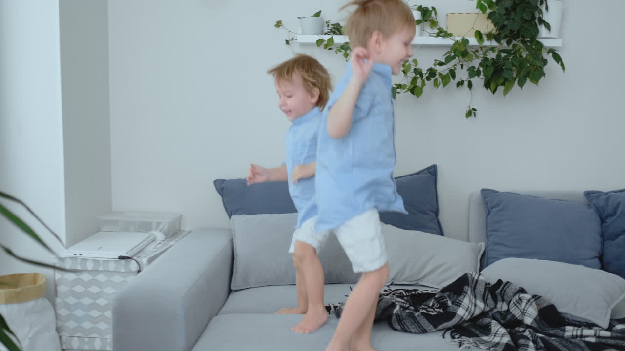 Two little boys jumping on the couch and having fun