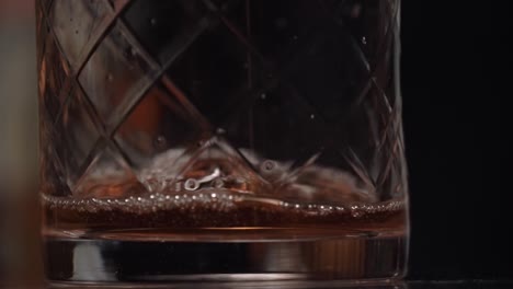 a bartender is pouring spirit and liquor into the stirring glass and start to stir along a lot of ice using a long copper bar spoon.