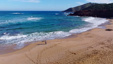 imágenes aéreas cinematográficas de una persona paseando a un perro por la playa en cala pilar, menorca españa