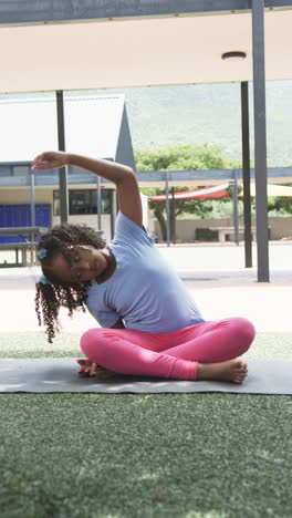 vertical video: in school, child stretching on yoga mat during outdoor physical education class