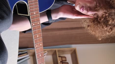 a young curly-haired musician with a guitar plays a calm sad melody. the young guitarist is tired.
