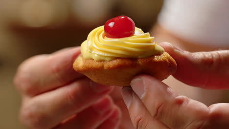 Close-up of Hands Holding a Small Dessert with Yellow Frosting and a Cherry