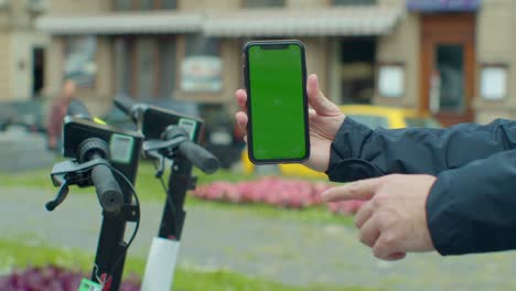 young man paying for electric scooter use app with green mock-up screen smartphone. green screen smartphone.