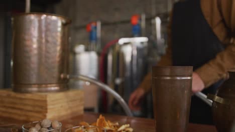 Caucasian-man-working-at-gin-distillery,-wearing-apron,-connecting-pipe-to-distillation-equipment