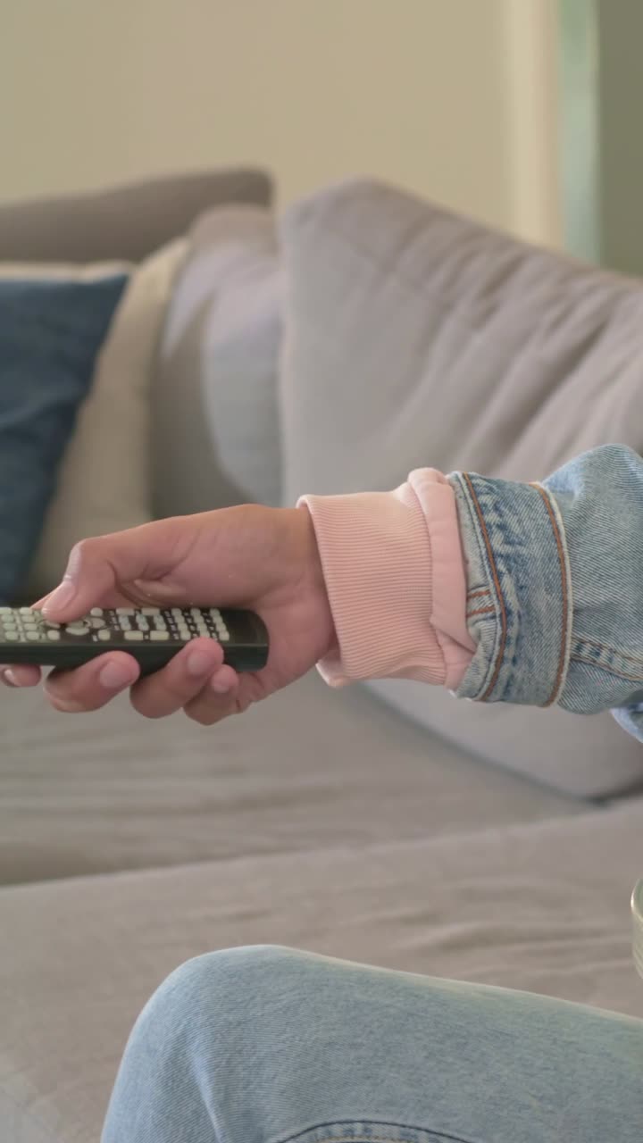 Video verticale: La telecamera si allontana, un uomo in jeans si allunga per prendere il telecomando tenendo i popcorn, con spazio per il testo.