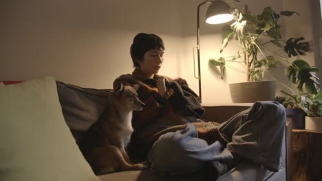 woman with dog on the couch knitting a piece of handmade clothing