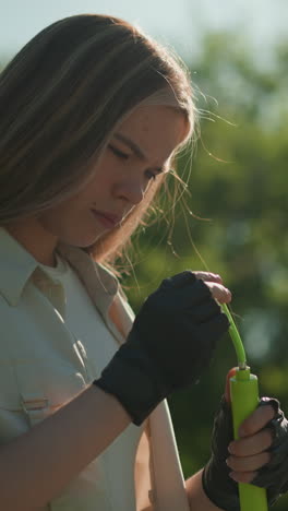 mujer enfocada se encuentra examinando la bomba de aire verde, profundamente en el pensamiento, contra un fondo sereno de árboles exuberantes y la luz del sol moteada en un día brillante