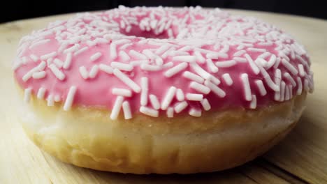 Macro-video-of-pink-donut-spinning-on-wooden-plate