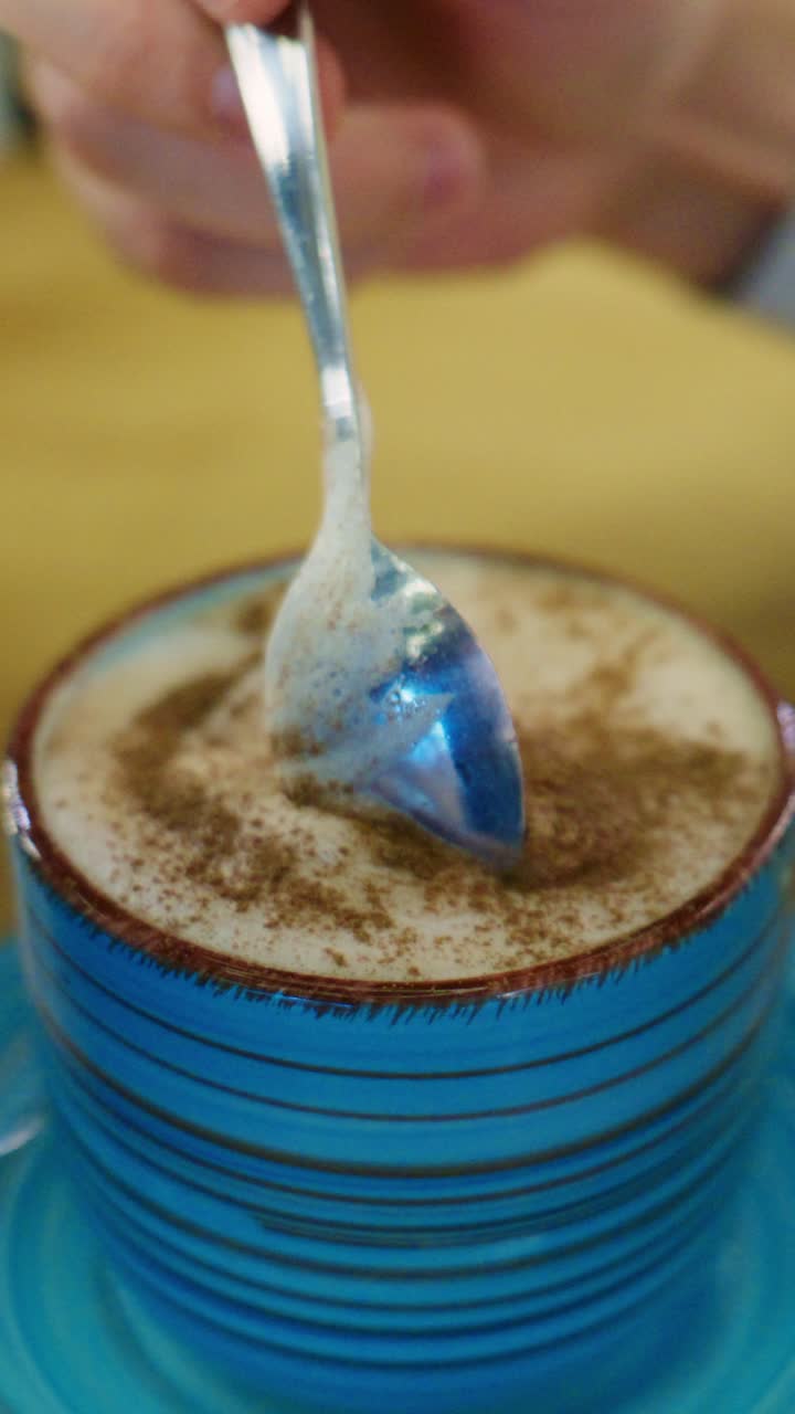 Un'esperienza all'aroma di caffè: mescolare un cappuccino preparato alla perfezione in una vivace tazza blu, arricchito da un pizzico di cannella su un tavolo accogliente.