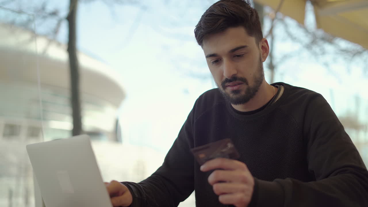 hombre enfocado con una tarjeta de crédito y usando una computadora portátil