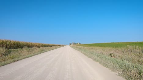 pov while driving past fields on a wide gravel road in rural iowa in late summer