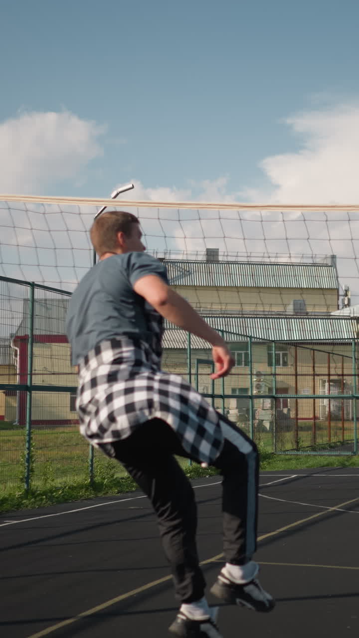 배구 훈련 세션에서 여자 운동 선수가 코치에게 공을 전달하고, 코치는 그것을 네트, 야외 스포츠 코트, 네트, 초록색, 멀리 배경에 있는 사람들로 니다.