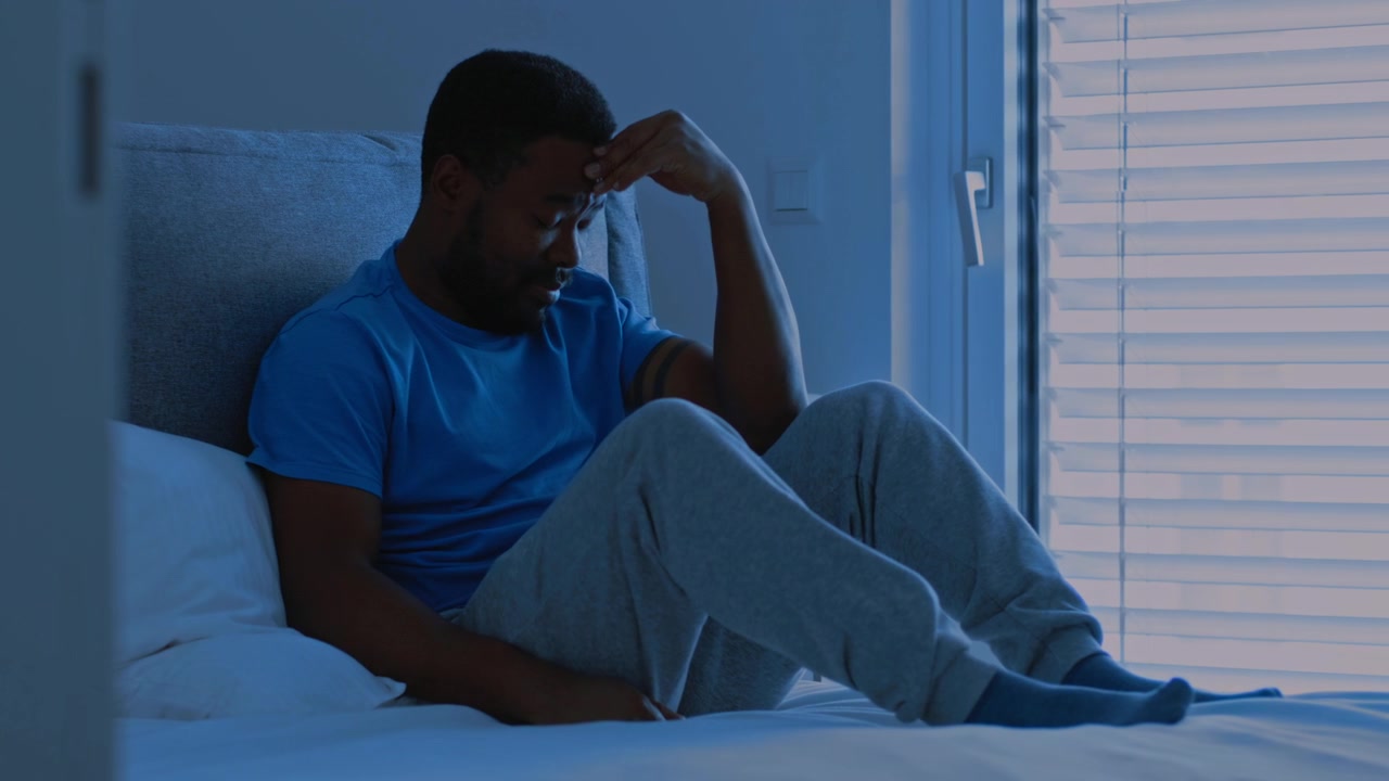 Stressed Man Sitting on Bed at Night