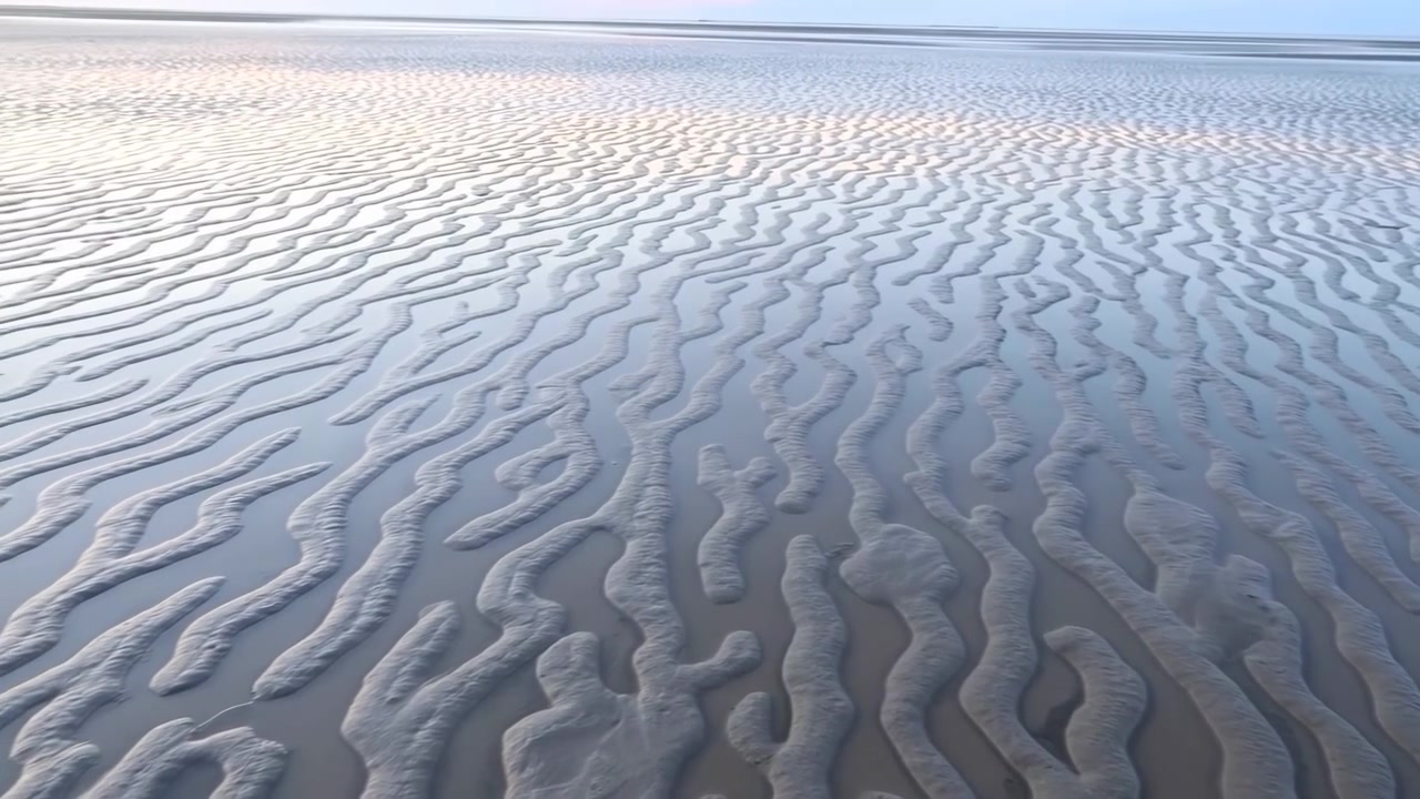 Mid-sequence low-tide coastal scene with rippled wet sand ridges stretching to distant horizon