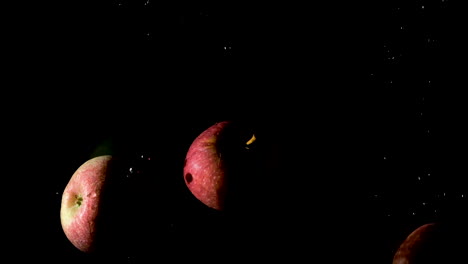 Red-apples-dropped-in-water-on-black-background,-slow-motion-close-up