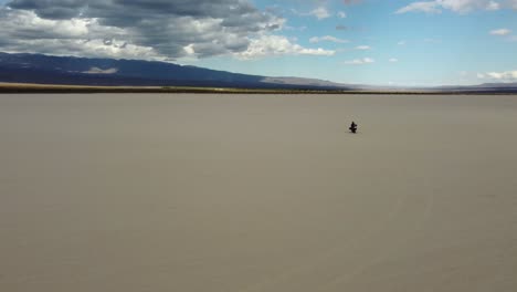 Rider-on-blue-motorcycle-approaches-camera-on-vast-flat-sandy-arroyo