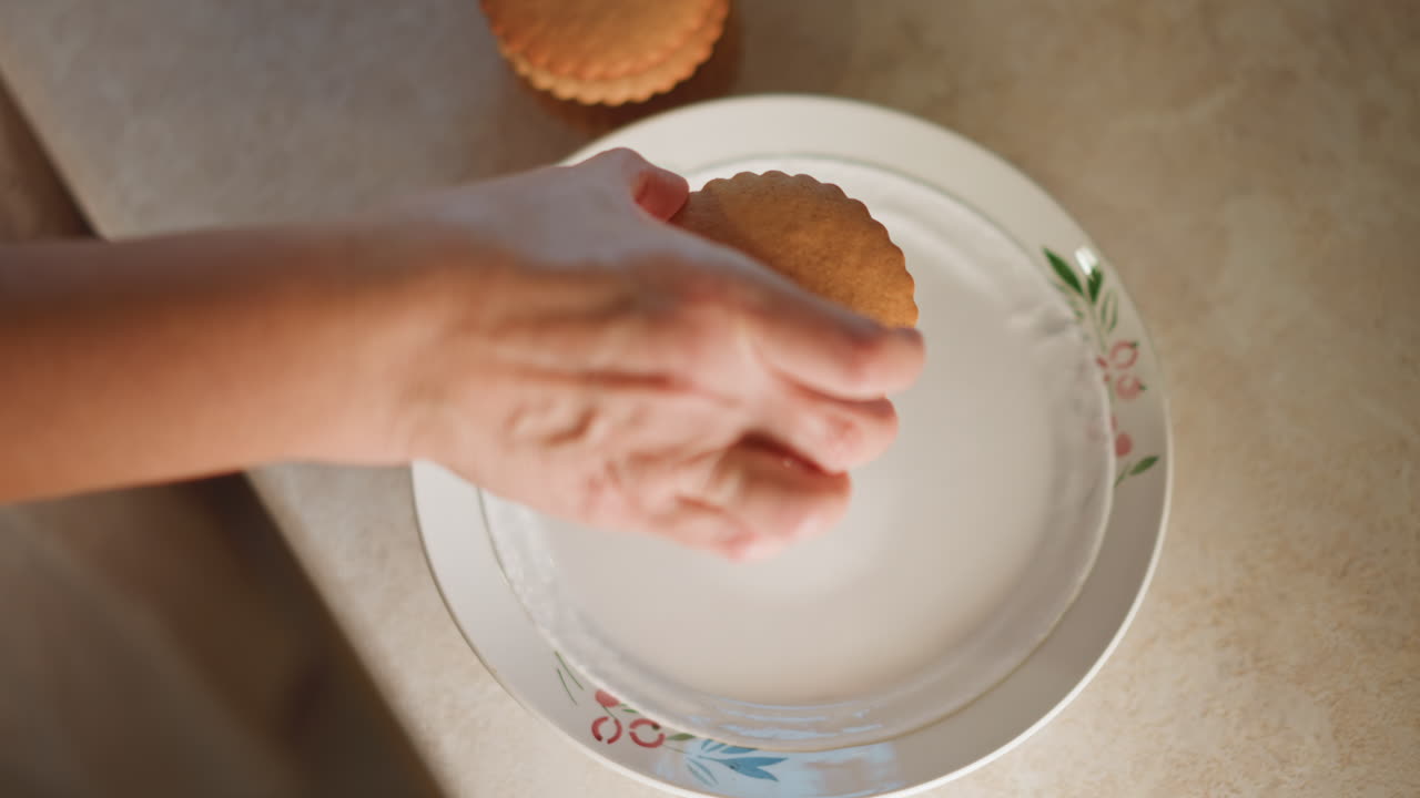 Closeup hand placing pumpkin pie tart on floral plate, gentle overhead motion, warm countertop light, focus on crust texture and homemade preparation, home baker arranging mini dessert for family
