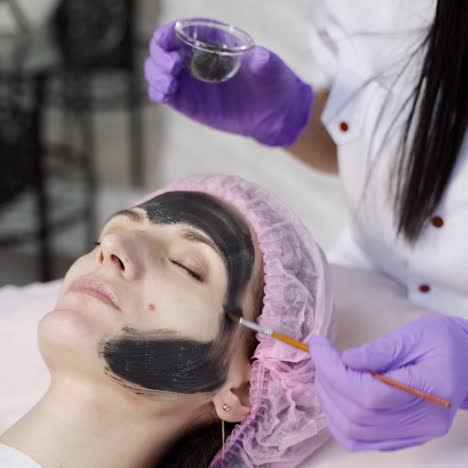 a doctor-cosmetologist applies a black mask with a brush to cleanse and moisturize the skin of the face in the beauty center. close-up.