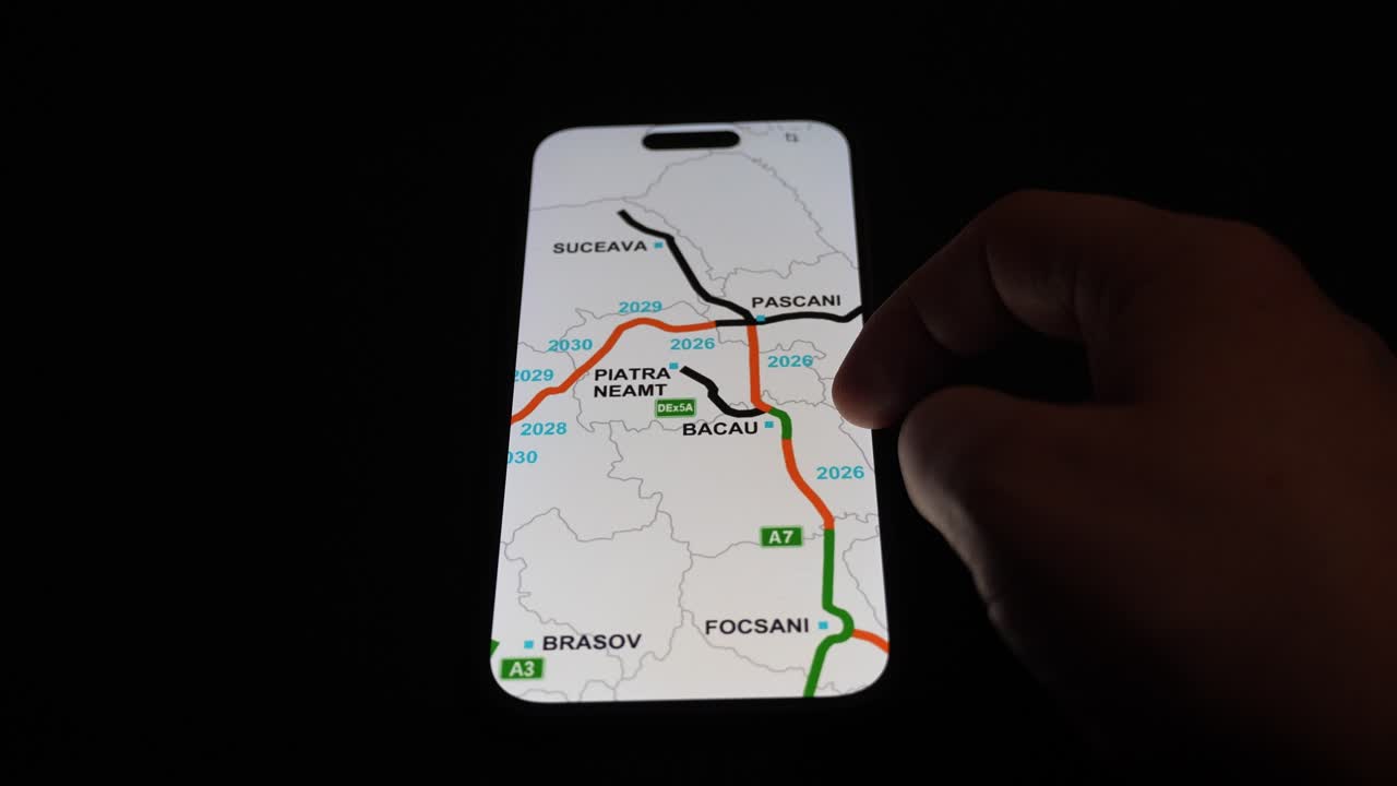 Hand holding smartphone and screen shows Romania A7 highway map with green route from Bucharest to Suceava