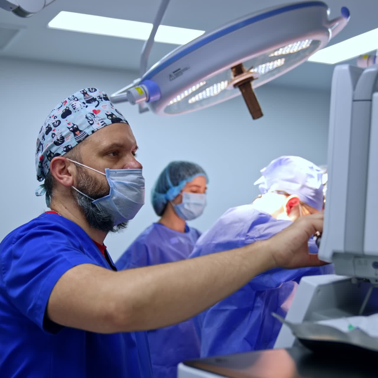 Surgery in progress in modern operational room. Male anesthesiologist looks at the screen of equipment and chooses the parameters on the sensor touch pad