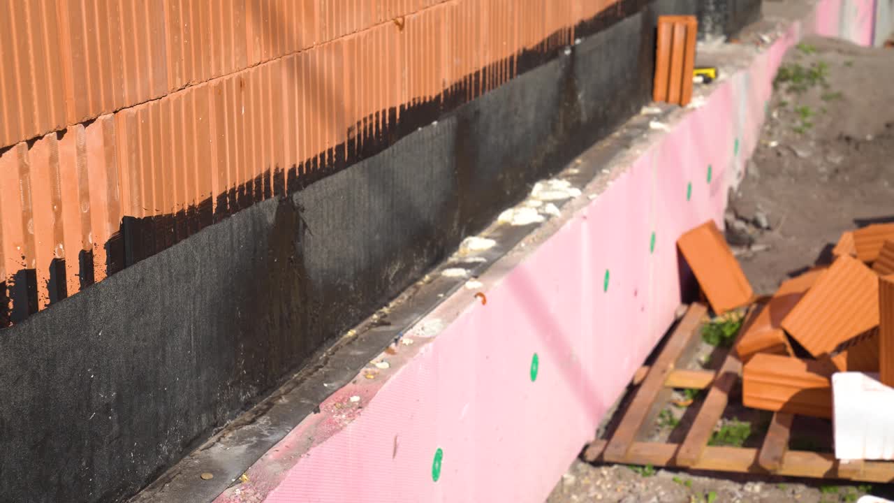 Insulation panels and bitumen sealing visible on house foundation and lower wall