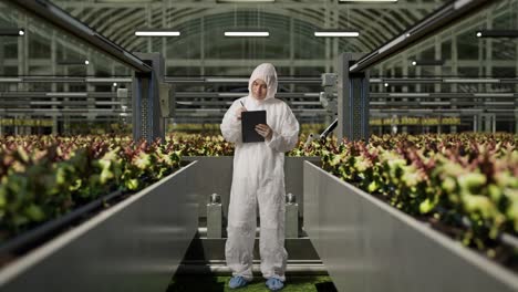 full body of asian man researcher looking around and taking note on a tablet while standing in the greenhouse with smart robotic farmers