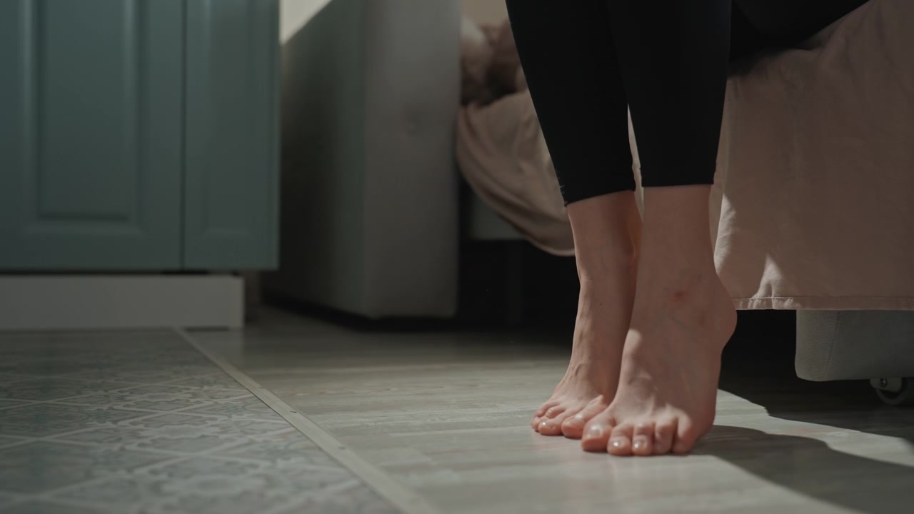 Bare feet on tile woman steps out of slippers and stands poised on cool floor, toes gripping tile, subtle light and casual leggings, closeup foot movement, quiet anticipation and gentle rhythm