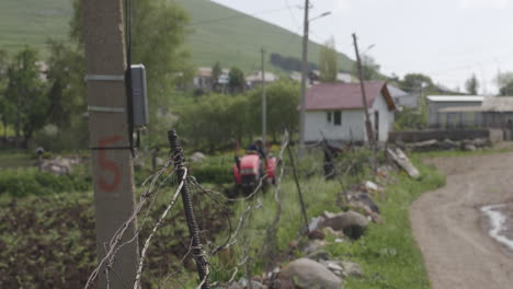 Defocused-Background-Of-Two-Men-At-Work-With-One-Driving-A-Red-Tractor-Plowing-The-Field-Next-To-A-Dirt-Road-On-A-Sunny-Day-In-A-Small-Village-Of-Moliti,-Georgia