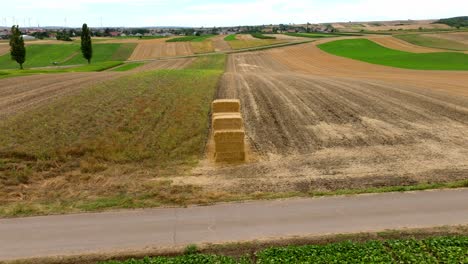 Luftaufnahme-Von-Quadratischen-Heuballen-Auf-Dem-Ackerland-Mit-Windpark-Im-Hintergrund