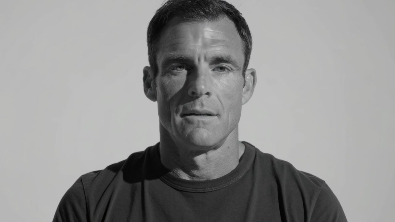 Answering off-camera question, man in dark tee speaking in studio with light backdrop and lighting