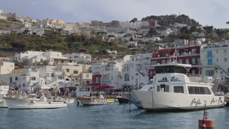 Port-or-harbor-of-Capri-island,-and-stunning-coastal-town-sprawls-up-mountain,-italy