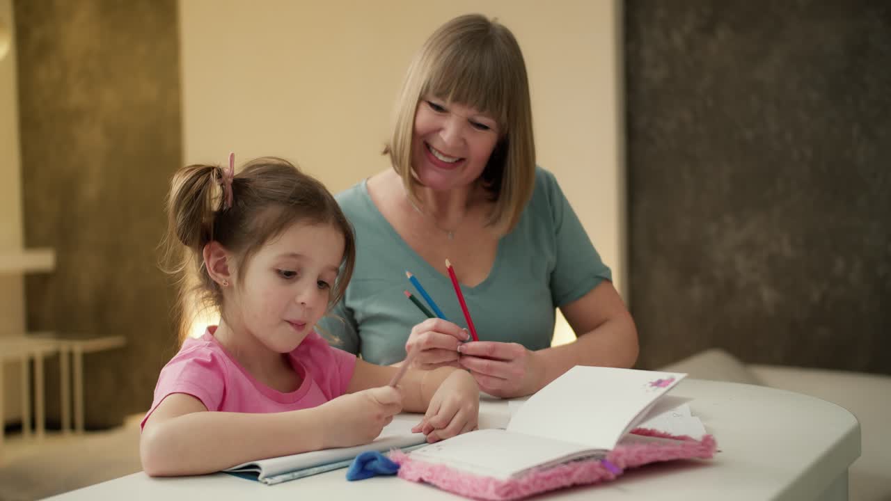 V Deo Premium Una Mujer De Mediana Edad Sonriente Sentada Con Su Peque A Nieta Coloreando