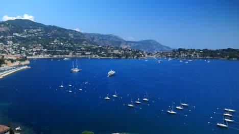 High-angle-pan-over-Villefranche-sur-Mer-azure-blue-bay,-French-Riviera,-France