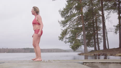 mujer emocional en togas se calienta con el método wim hof en el pontón después de un baño de hielo