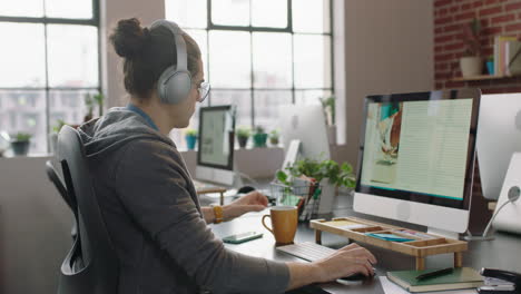 young businessman working on graphic design project using computer listening to music enjoying checking smartphone messages drinking coffee in relaxed office workplace