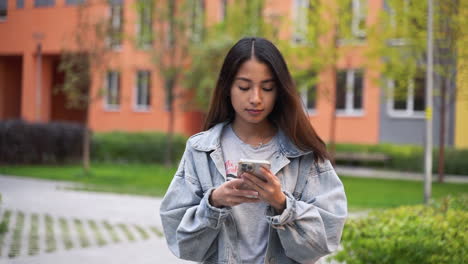 beautiful young japanese girl texting on mobile phone while walking towards camera outdoors