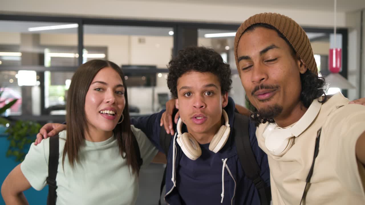 Amici studenti afroamericani in posa nella hall, l'amico a destra che estende il braccio tiene il telefono esultando