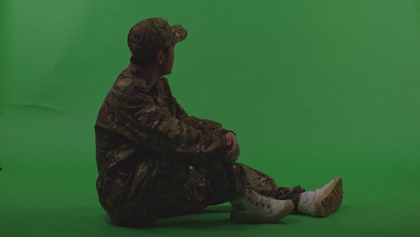 full body of asian male soldier sitting and looking around with serious facial expression to protects his country from the war on the green screen background