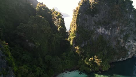 aerial-drone-flying-between-two-limestone-cliffs-of-Ko-Poda-Island-with-a-secret-white-sand-beach-and-white-yacht-anchored-in-the-harbor-of-the-beautiful-turquoise-blue-ocean-in-Krabi-Thailand