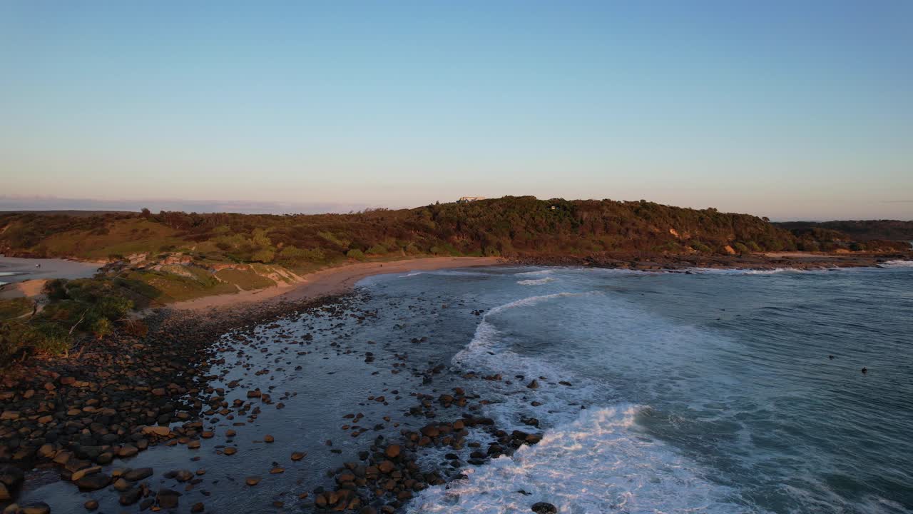 olas chocando contra las rocas y guijarros en la playa de angourie point durante la puesta de sol en yamba, nsw, australia