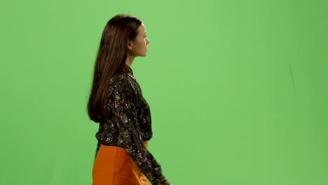 una joven morena casual está caminando en una maqueta de pantalla verde en el fondo.