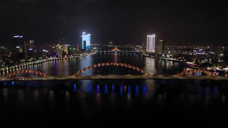 Amazing-colorful-wide-aerial-shot-of-iconic-Dragon-Bridge-Cau-Rong,-traffic-and-city-skyline-at-night-in-Danang,-Vietnam