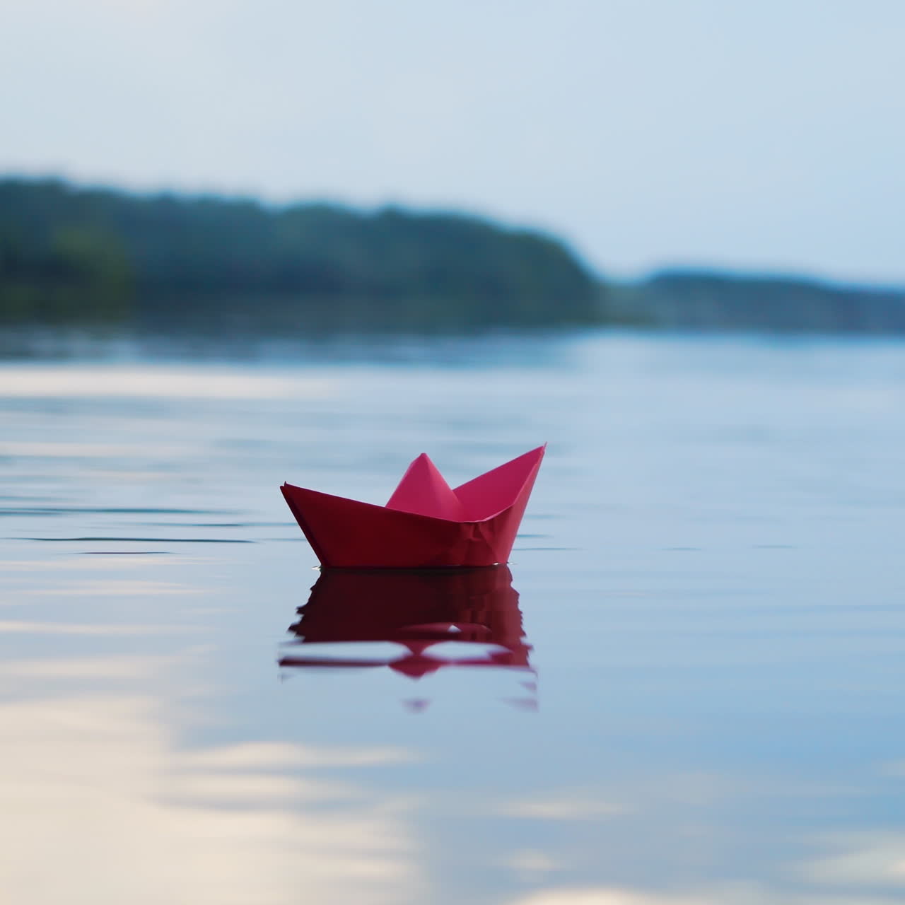 Alone homemade ship spinning on the evening river on the beautiful natural background. One red paper boat floating on the water surface