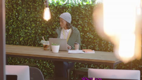 Joven-Mujer-De-Negocios-Afroamericana-Usando-Una-Computadora-Portátil-Navegando-En-Línea-Escribiendo-Mensajes-Tomando-Café-Escuchando-Música-Revisando-El-Teléfono-Inteligente-En-Un-Moderno-Lugar-De-Trabajo-De-Oficina