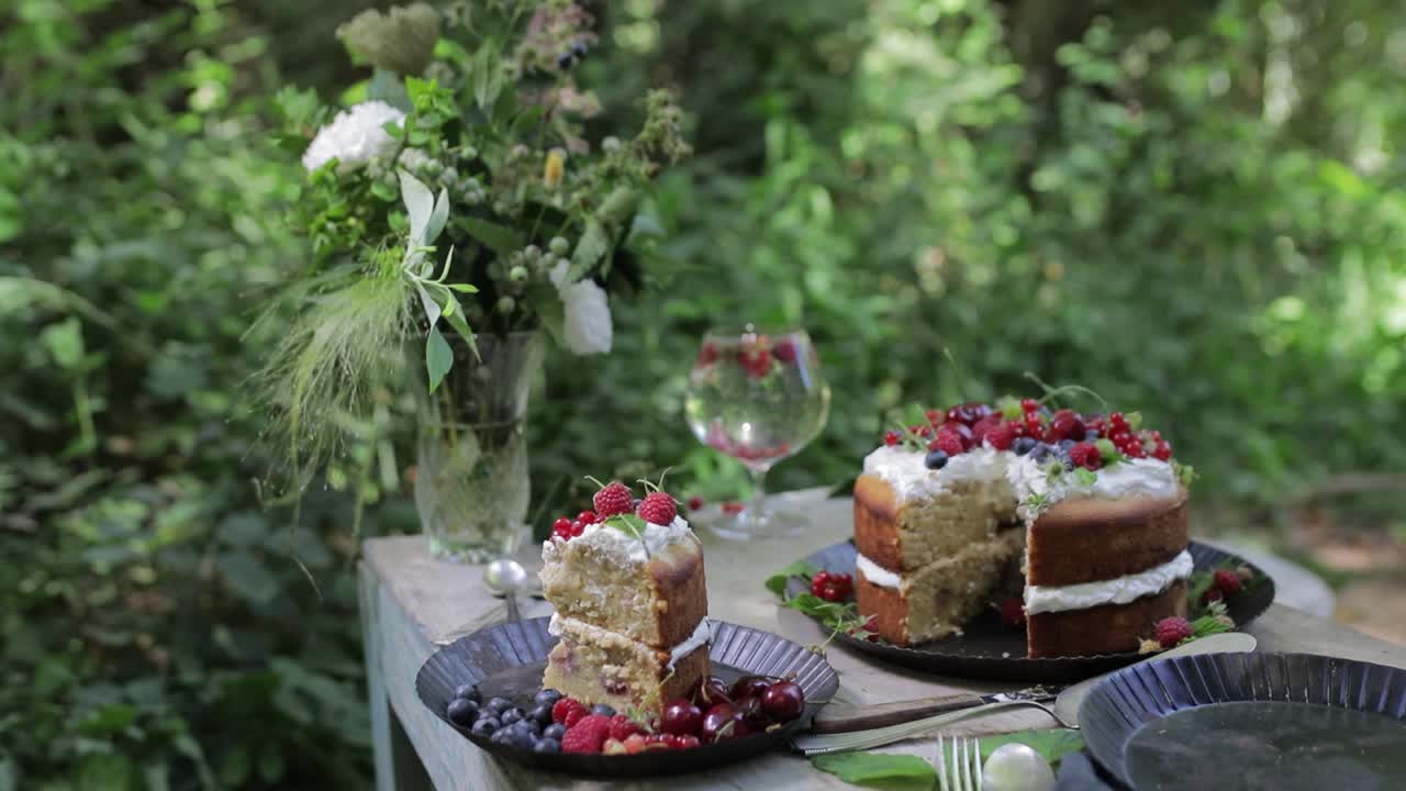 Bredt billede af en lækker bærcremekage og et stykke serveret på et rustikt bord i en frodig grøn have under en sommer eftermiddagsfest