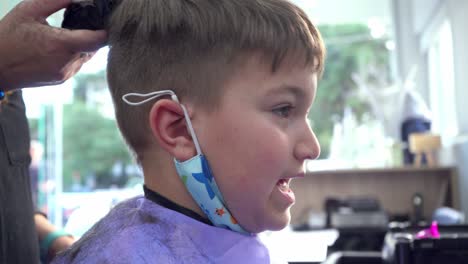 Close-up,-side-view-shot-of-caucasian-boy-getting-a-haircut-from-professional-hair-dresser,-using-a-trimmer