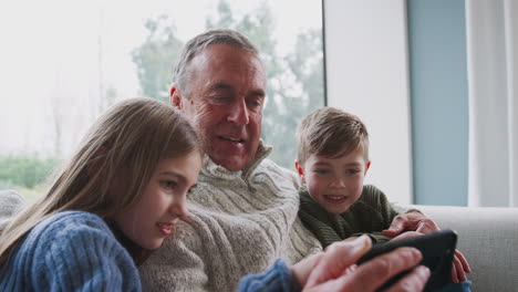 abuelo jugando videojuegos con los nietos en el teléfono móvil en casa