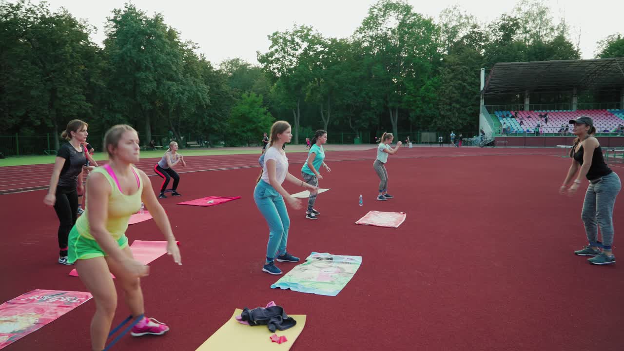 Female team training on the outdoor stadium. Group of women doing exercises with fitness rubber on the modern sports ground. Healthy lifestyle.