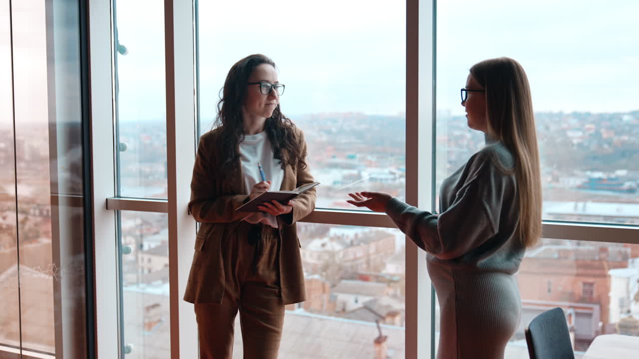 Business communication in the office, exchanging ideas, brainstorming, finding solutions. Two ladies in office cheerfully talk.